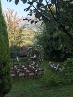 An outdoor wedding venue with wooden chairs arranged in rows, a floral arch, and a backdrop of trees and hills.