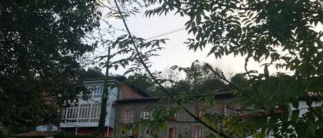 Un edificio tradicional con fachada de piedra y marcos de ventanas rojos, rodeado de exuberante follaje y un césped bien cuidado.