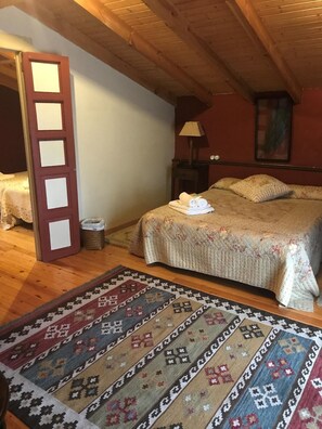 A bedroom with a wooden ceiling, a bed with a floral bedspread, a bedside table with a lamp, and a patterned rug. - Hotel Palacio De Libardon (Colunga)