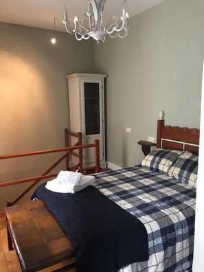 Um quarto com uma cama, um banco de madeira, um guarda-roupa e um candelabro.