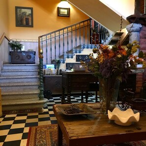 A checkered floor, a wooden table with a vase, a staircase with blue balusters, and a wall-mounted picture. - Hotel Palacio De Libardon (Colunga)