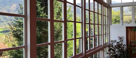 A room with large windows offering a view of a mountainous landscape. There are wooden chairs and a potted plant inside.