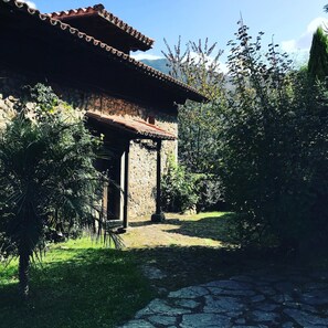 A rustic stone building with a tiled roof, surrounded by lush greenery and a cobblestone path. - Hotel Palacio De Libardon (Colunga)