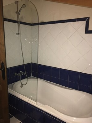 Un bagno con una vasca da bagno bianca, pareti piastrellate di blu e un angolo doccia.
