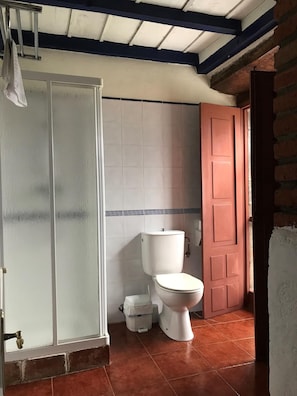 Un baño con un inodoro blanco, zona de ducha y una puerta roja.