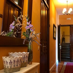 A hallway with a wooden door, a mirror, a vase with flowers, and a decorative bowl on a console table. - Hotel Palacio De Libardon (Colunga)