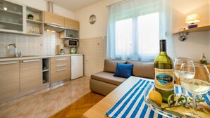A modern kitchen with a dining area, a bottle of wine, and glasses on a table. - Mediterranean apartment with pool, barbecue, loungers - only 400 meters to the beach (Baska)