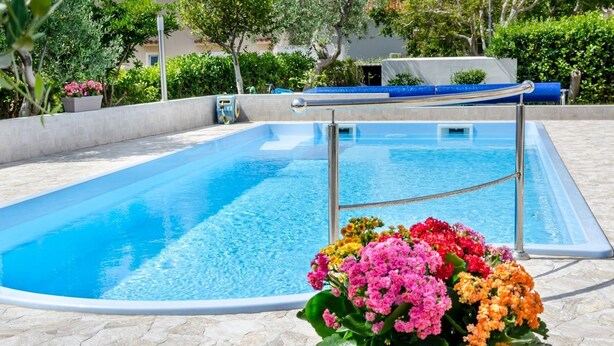 A swimming pool with a metal ladder, surrounded by a stone deck and colorful flowers. - Mediterranean apartment with pool, barbecue, loungers - only 400 meters to the beach (Baska)