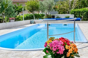 A swimming pool with a metal ladder, surrounded by a stone deck and colorful flowers. - Mediterranean apartment with pool, barbecue, loungers - only 400 meters to the beach (Baska)