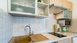 A modern kitchen with a sink, stainless steel faucet, a microwave, a kettle, and a cabinet with a glass door. - Mediterranean apartment with pool, barbecue, loungers - only 400 meters to the beach (Baska)
