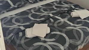 Una cama con un estampado abstracto en blanco y negro, una mesita de noche con una lámpara y una toalla blanca doblada sobre la cama.