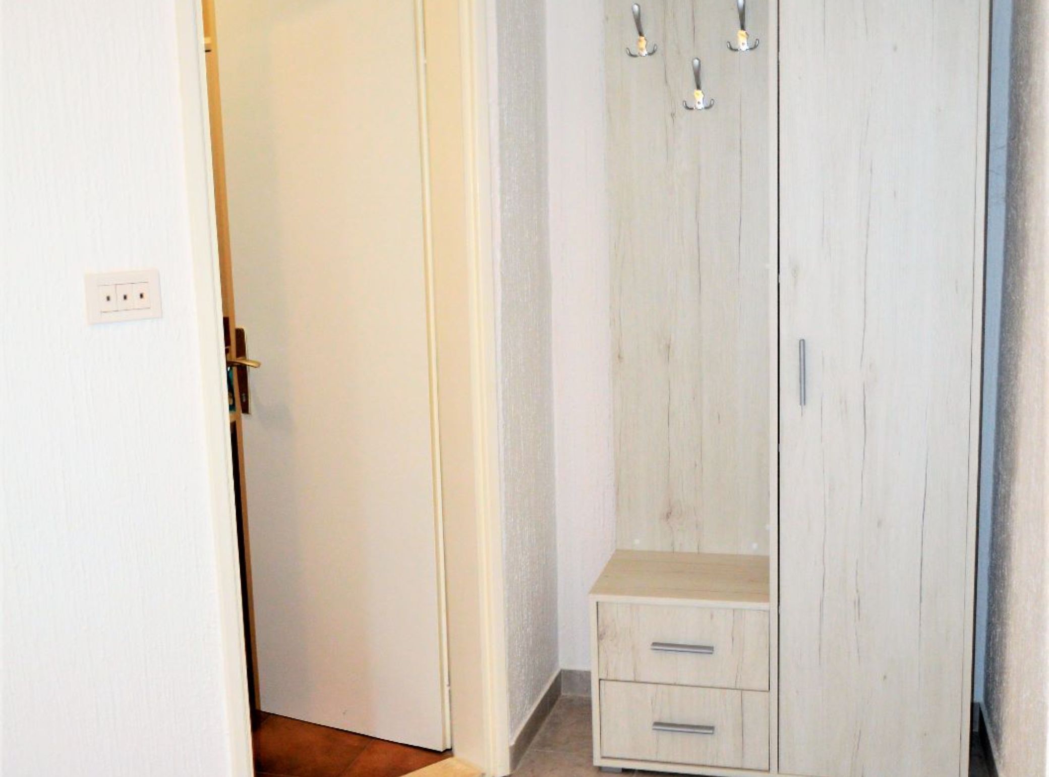 A room with a wooden wardrobe, a small bedside table, and a door.