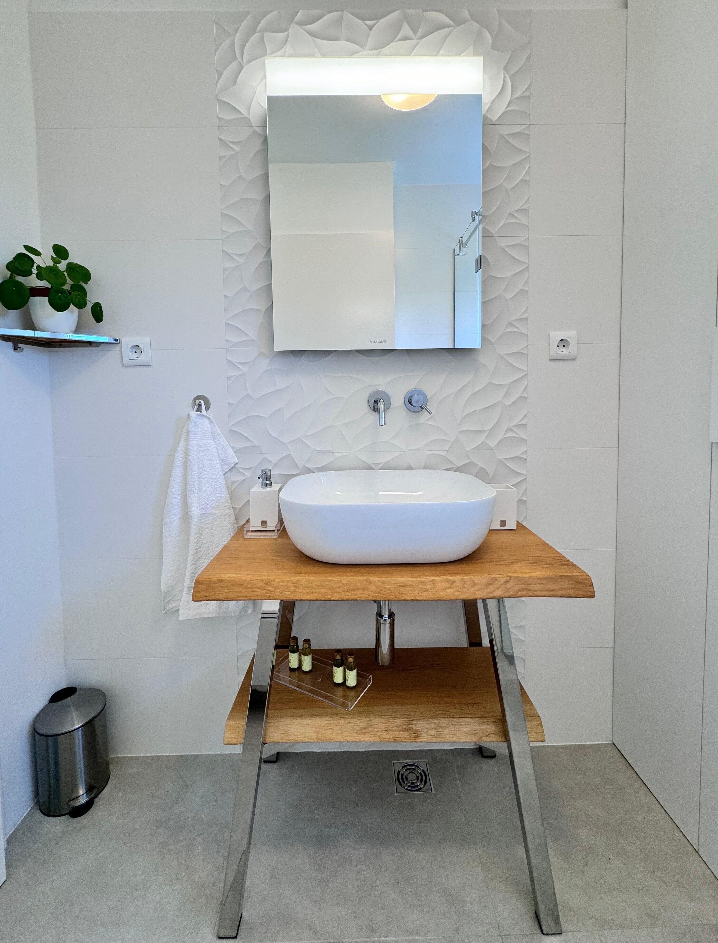 Een moderne badkamer met een witte wastafel, een houten aanrechtblad en een decoratief wandpaneel.