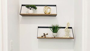 Un couloir avec deux étagères en bois fixées au mur, chacune contenant des objets décoratifs et des plantes. Un banc bleu rembourré est placé au centre du couloir.