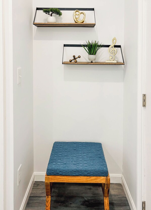 A hallway with two wooden shelves mounted on the wall, each holding decorative items and plants. A blue cushioned bench is placed in the center of the hallway.