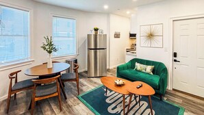 Un espace de vie compact comprenant un coin repas, une kitchenette, un canapé vert et une porte dotée d’un système de verrouillage à clavier.