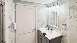 Une salle de bain avec une porte blanche, un lavabo surmonté d’un miroir et des murs à motifs de marbre.