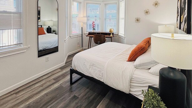 Une chambre à coucher avec un lit, un bureau, un miroir et une fenêtre avec des stores.