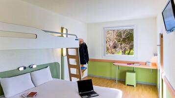 Habitación de hotel moderna con literas, un escritorio con una silla, una computadora portátil y una ventana con vistas a árboles.