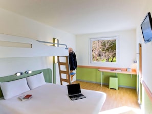 A modern hotel room with a bunk bed, a desk with a chair, a laptop, and a window with a view of trees. - Ibis Budget Madrid Alcala de Henares (Alcala de Henares)