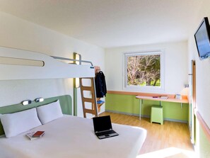 Ein modernes Hotelzimmer mit Etagenbett, Schreibtisch mit Stuhl, Laptop und Fenster mit Blick auf Bäume.