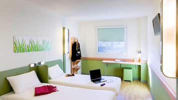 Habitación de hotel con dos camas, un escritorio con una computadora portátil, una ventana con vista y un perchero con una chaqueta.
