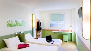 Habitación de hotel con dos camas, un escritorio con una computadora portátil, una ventana con vistas y un perchero con una chaqueta.