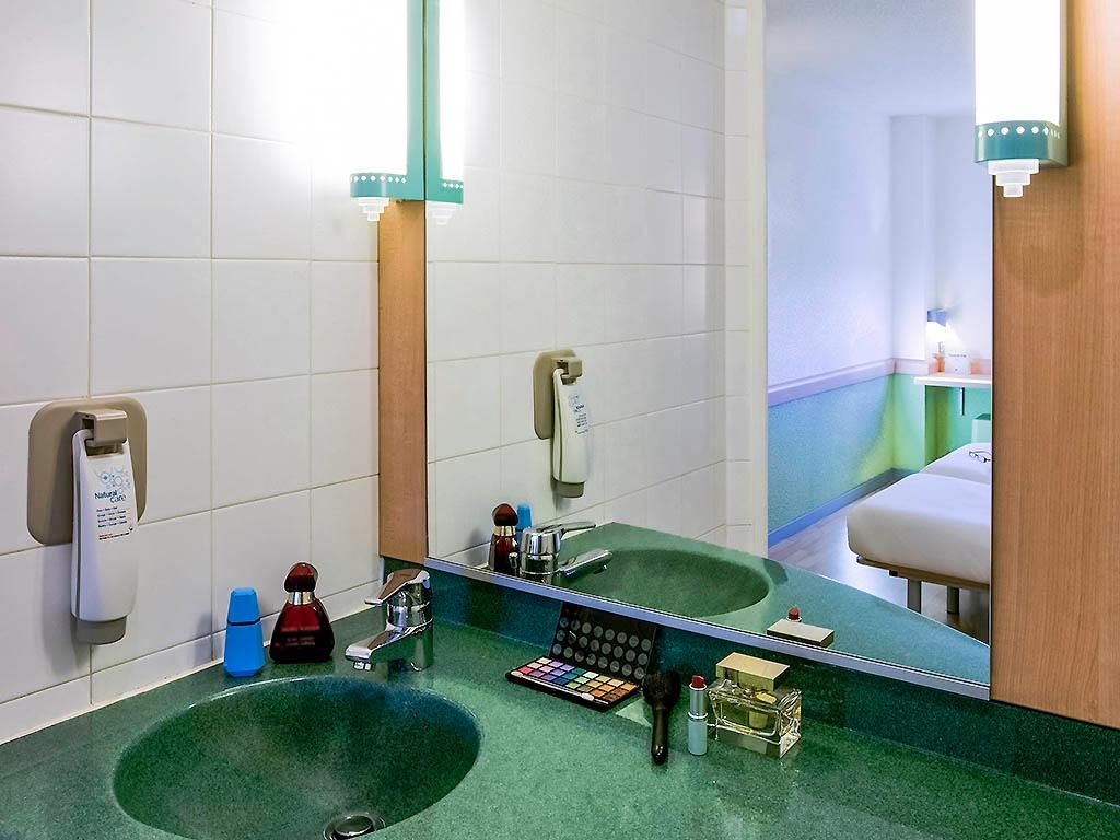 Un baño con un lavabo verde, un espejo y distintos artículos de aseo.