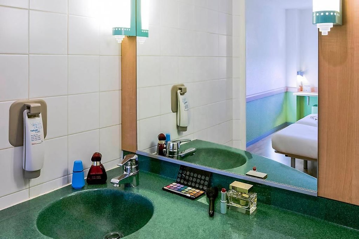 A bathroom with a green sink, a mirror, and various toiletries.