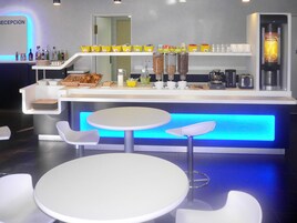 A modern bar area with a reception desk, seating, and various food and drink dispensers.