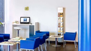 A hotel reception area with a computer monitor, a desk, and several blue chairs. - Ibis Budget Madrid Alcala de Henares (Alcala de Henares)
