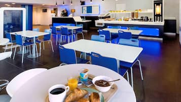 Un área de desayuno moderna con mesas, sillas, una recepción y una máquina de café.