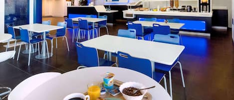 Un espace moderne dédié au petit-déjeuner, avec des tables et des chaises, un comptoir de réception et une machine à café.