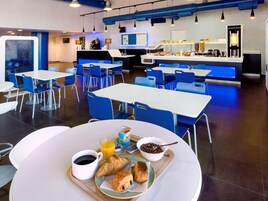 A modern breakfast area with tables and chairs, a reception desk, and a coffee machine.