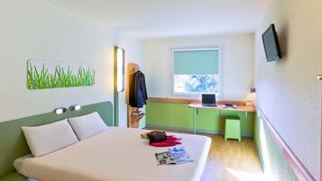 Habitación de hotel con cama, escritorio, silla, televisor y ventana con vista a árboles.