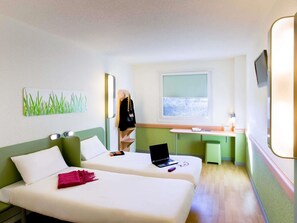 Ein Hotelzimmer mit zwei Betten, einem Schreibtisch, einem Laptop und einem Fenster mit Blick.