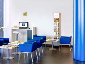 Zona de recepción de hotel con un monitor de computadora, un escritorio y varias sillas azules.