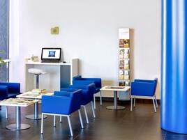 A hotel reception area with a computer monitor, a desk, and several blue chairs.