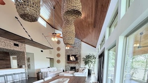 A spacious living area with a long wooden table, white sofas, a stone fireplace, and large windows. - Ultimate Lake Resort Xtravaganza | Lake Conroe | April Sound (Montgomery)