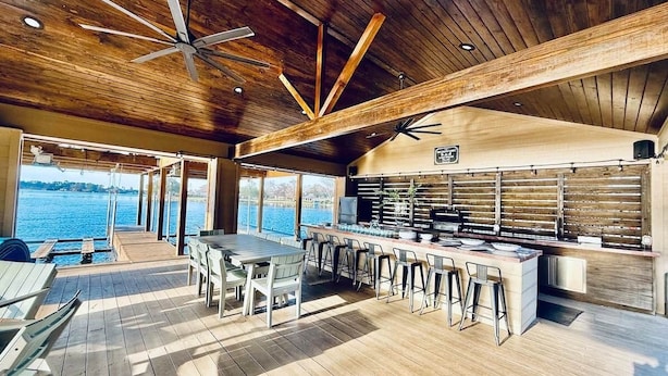 A spacious outdoor kitchen area with a long counter and bar stools, overlooking a body of water. - Ultimate Lake Resort Xtravaganza | Lake Conroe | April Sound (Montgomery)