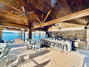 A spacious outdoor kitchen area with a long counter and bar stools, overlooking a body of water. - Ultimate Lake Resort Xtravaganza | Lake Conroe | April Sound (Montgomery)