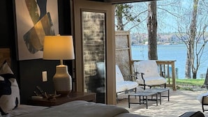 A bedroom with a large bed, a bedside lamp, a chair, and a view of a lake. - Ultimate Lake Resort Xtravaganza | Lake Conroe | April Sound (Montgomery)