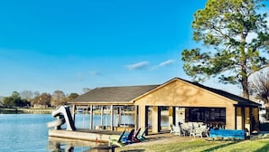 A lakeside building with a covered patio, outdoor seating, and a dock. - Ultimate Lake Resort Xtravaganza | Lake Conroe | April Sound (Montgomery)