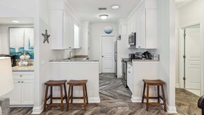 A kitchen with white cabinets, a central island, two stools, a microwave, and a refrigerator.