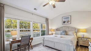 A bedroom with a large bed, a desk, a chair, a nightstand, and a ceiling fan.