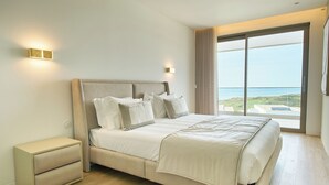 A modern bedroom with a large bed, bedside tables, and a view of the ocean.