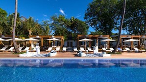 A poolside area with lounge chairs and umbrellas, surrounded by trees and wooden structures.