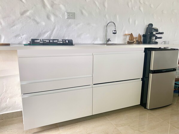A modern kitchen with white cabinetry, a stainless steel refrigerator, a coffee maker, and a small sink.