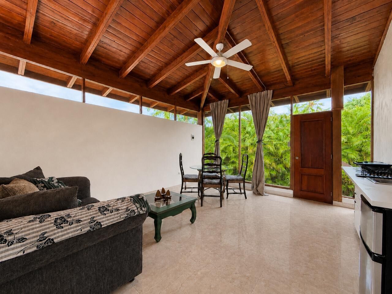Une pièce avec un plafond en bois, un canapé, une table à manger avec des chaises et une vue sur la verdure à l’extérieur.