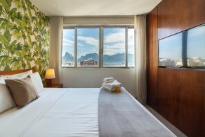 A hotel room with a large bed, a TV, a window with a city view, and a tropical wallpaper. - 10 Minutes From Ipanema Beach Ac1007 (Rio de Janeiro)